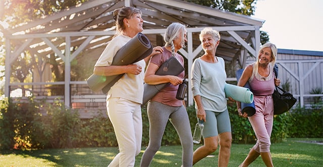 Four women walking outside carrying yoga mats