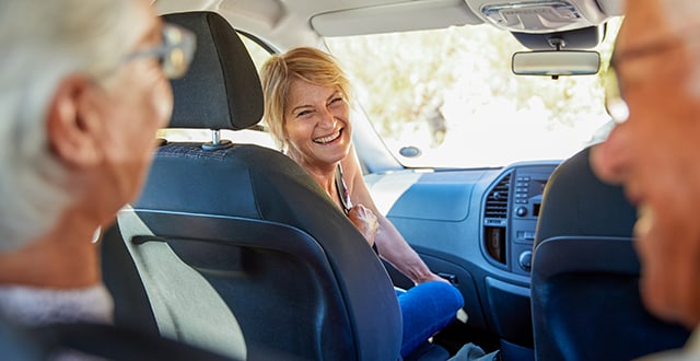 Woman in driver's seat smiling at senior passengers in back seat